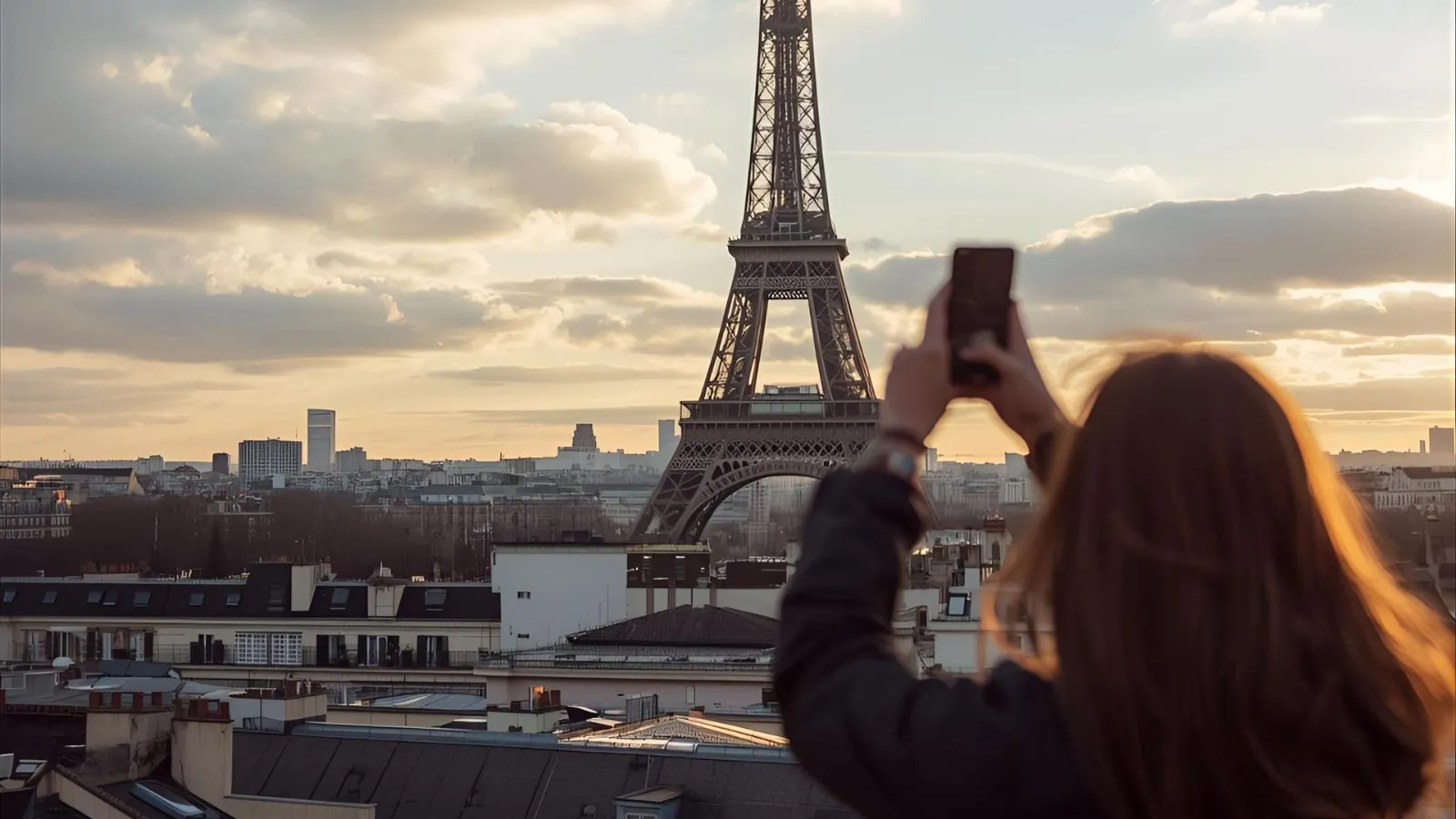 Traveler taking a photo of the Eiffel Tower over the Seine at sunset.