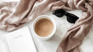Minimal flat-lay with coffee, sunglasses, scarf, and journal.