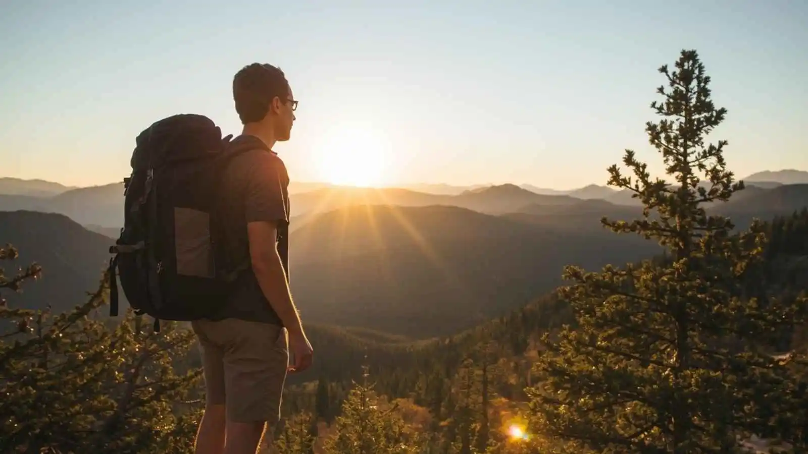 Hiker with a backpack on a ridge at sunrise.