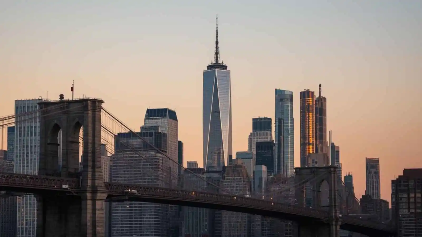 Golden-hour New York City skyline with a bridge in the foreground.
